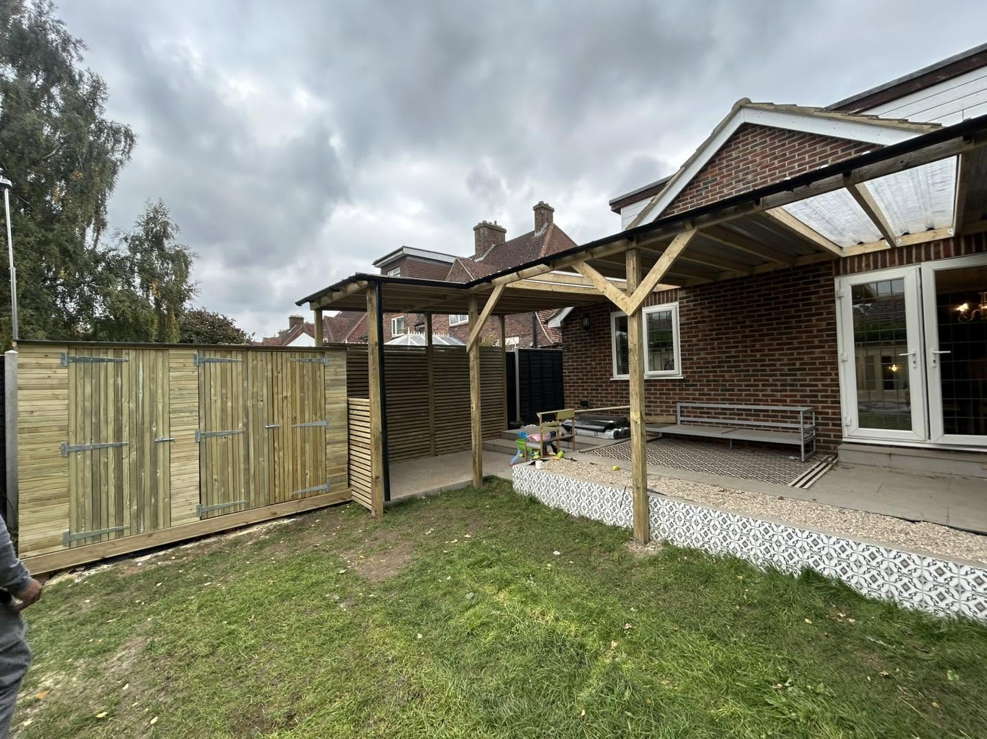 Timber pergola with a covered roof beside a brick house